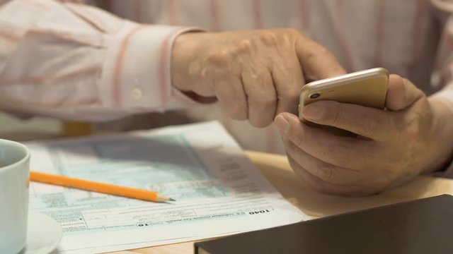 Elderly Man Text Messaging On Smartphone And Tax Form 1040