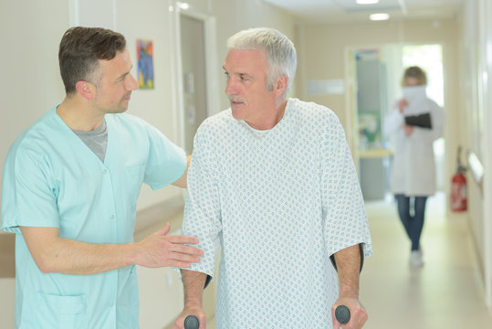 Male Doctor Is Helping Older Patient With Crutches