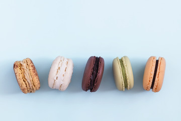 Row of colorful french macaroons on blue background. Top view, copy space for text. Social media, blogging concept 