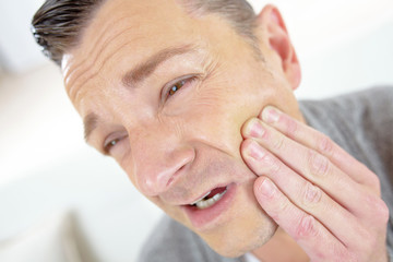 man holding his swollen jaw expressing a tooth acke