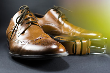 Beautiful brown leather men's shoes. Fashionable shoes isolated on black background. Brown leather belt. Lens flare in the background.