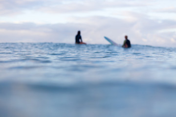 Two out of focus surfers sit in the distance on their surfboards as they wait for a wave to appear...