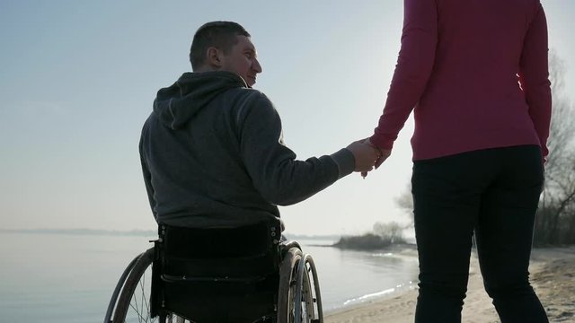 invalid love, handicapped gives hand to girlfriend, back view, cripple near river on wheel chair, male on wheelchair, man outdoors, disabled on nature, happy invalid self-confidence, sun glare