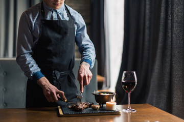 man slicing cooked medium rib eye steak on board, wide photo