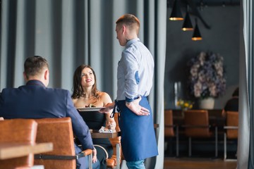 Positive young waiter serving terrace restaurant guests at table.Focus on the man
