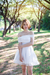 Portrait of Beautiful thai woman in white dress gold hairs stand  under tunnel tree in the sunny day,bright sunlight