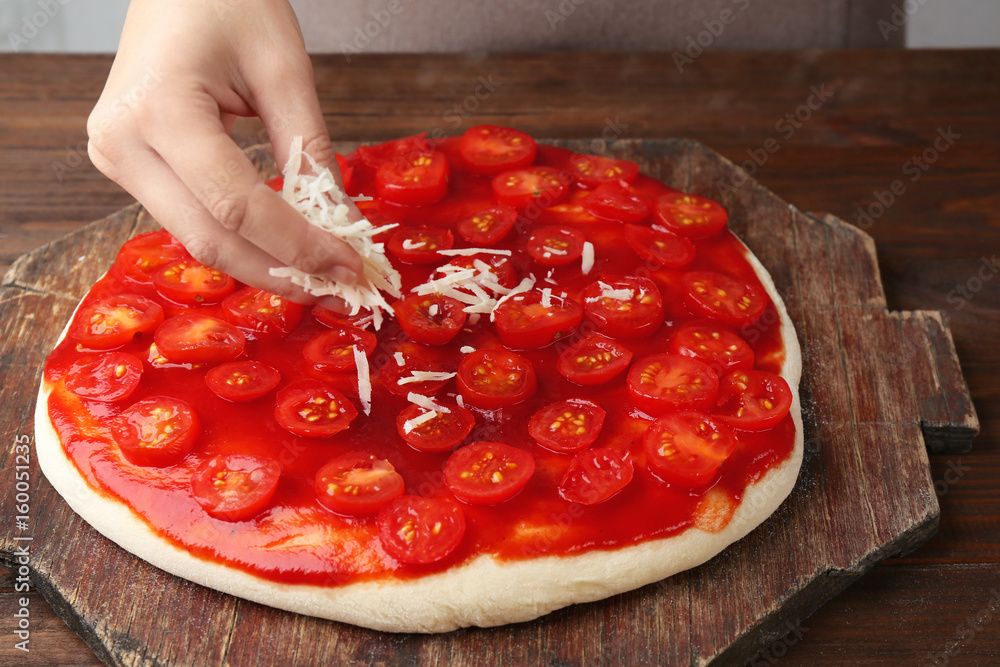 Wall mural Female hand making tasty traditional pizza on wooden board