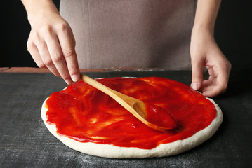 Female hands making traditional pizza on black table, close up