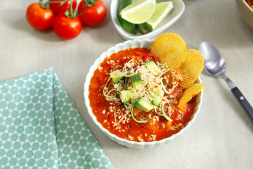 Bowl with delicious chili turkey, avocado slices, grated cheese and chips on table