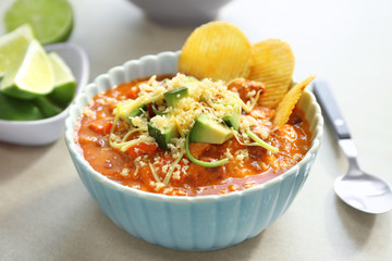 Bowl with delicious chili turkey, avocado slices, grated cheese and chips on table