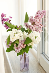 Glass vase with beautiful lilac flowers on window sill