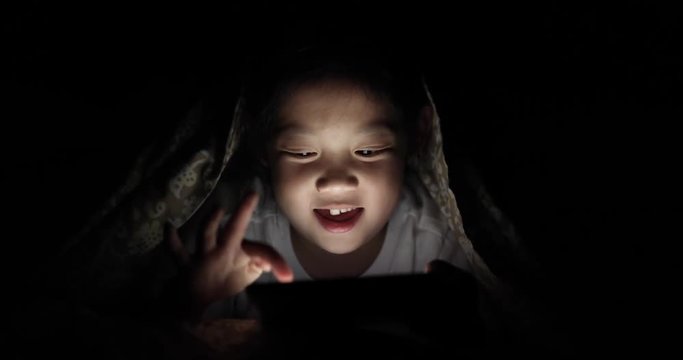 Asian Child Playing Game on Tablet PC in Bed at Night