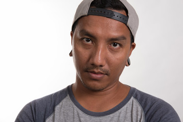 attractive asian man standing against a white background wearing gray t-shirt and cap and looking at camera.