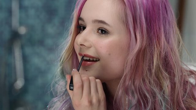 Young woman in puberty with pink hair is trying lip gloss at her lips