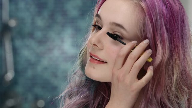 Young woman in puberty with pink hair is trying mascara at her eyelashes