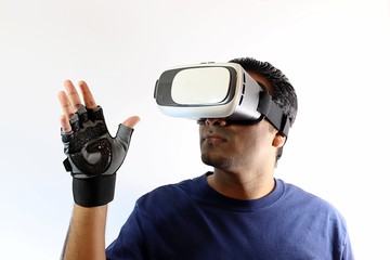 Young man wearing virtual reality goggles while standing against white background