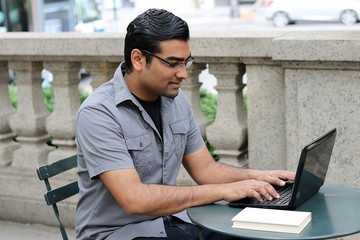 Happy business man typing on computer while sitting in urban park