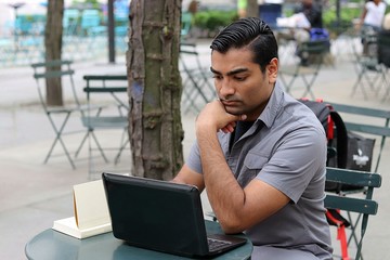 Student reading and working on laptop while sitting outside in city park