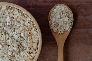Oat flakes or oatmeals in wood bowl put on rustic wood table. Rolled oat is clean food for health lover people. Prepare oat flakes for bakery or cooking. Natural organic food in vintage style concept.