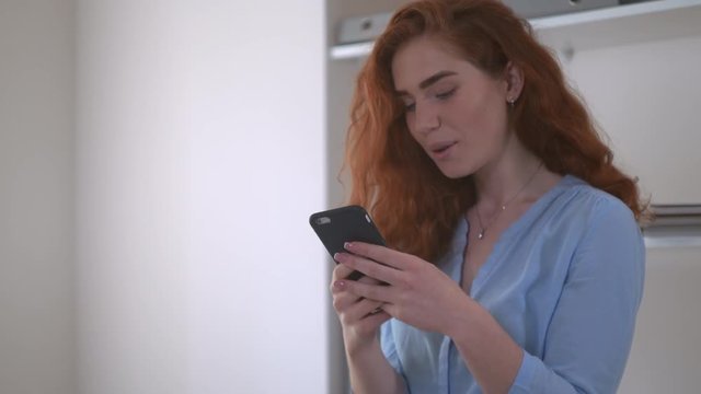 redheaded girl chatting smiling using smartphone. Woman with curly red hair using app on mobile phone for chatting in social net.