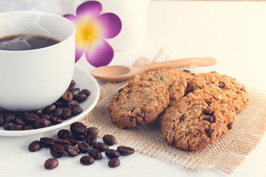 close up cup of coffee,milk,sugar,chocolate chip cookies ,coffee beans and flower on white wooden background with loft wall style with light in concept relax time