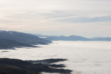 Naklejka na ściany i meble A valley filled by a sea of fog, with some hills resembling cliffs on the sea