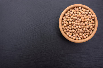 Peeled chickpeas lies in a wooden cup on a stony black board, black background, space for text