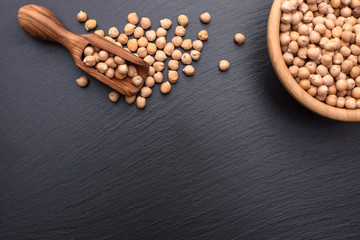 On a black stone board there is a wooden scoop and a wooden bowl with chickpeas, place for text