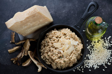 Risotto with porcini mushrooms in a cast-iron frying pan and its cooking ingredients. Top view on a...