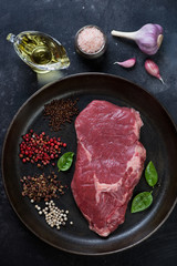 Top view of raw ribeye beefsteak with seasonings on a metal plate, vertical shot