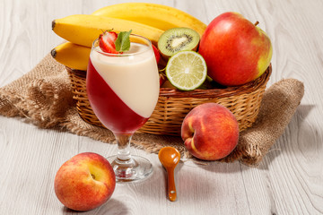 Cherry and milk jelly with strawberry piece in the glass, fresh strawberries, nectarine, lime, kiwi, banana, apple in a wicker basket on the table
