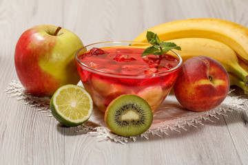 Cherry jelly with strawberry pieces in the glass bowl topped mint leaves and fruits on the white napkin