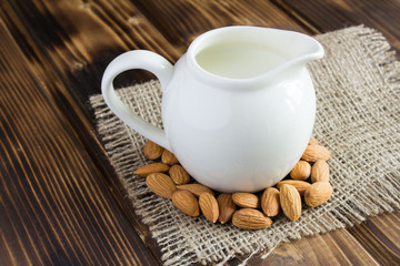 Milk in the ceramic jug and nuts on the wooden background