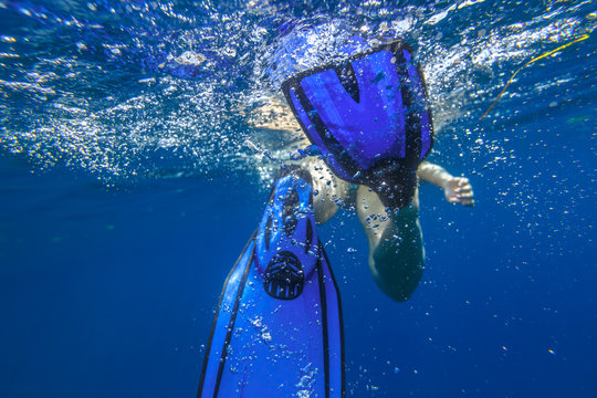 Closeup of blue fins of underwater female apnea while swimming. Bubbles of water. View from behind snorkeler woman in underwater activity. Watersport and leisure concept. Fins slamming into sea.