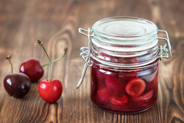 Jam from sweet cherries in a glass jar with lid on wooden background.