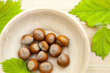 hazelnuts in a wooden bowl with green leaves on wooden background