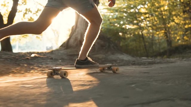 Evening sundown shot low section of teenager boy riding longboard in the park against sun, 120FPS slowmotion
