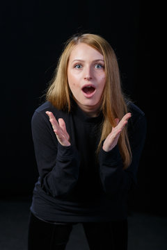 Surprised young blonde spread her hands in the sides on a black background