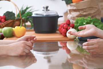 Close-up of human hands are gesticulate over a table in the kitchen. Women choosing menu or making online shopping. So much ideas for tasty cooking. Vegetarian, healthy meal and friendship concept