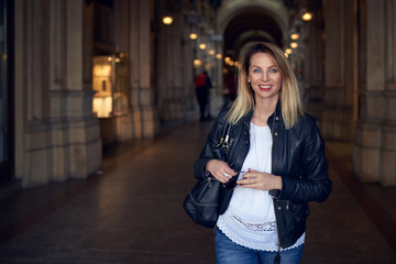 Attraktive schlanke blonde Frau kommt aus einer Einkaufspassage und lächelt