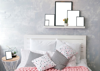 White and colored pillows on woodenl bed with white headboard. Shelf with photo frames with blank empty white cards above the bed with set of pillows and pink merino wool blanket