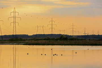 High-voltage poles reflected in the water of a lake