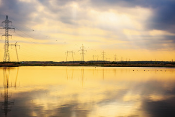 Fototapeta na wymiar High-voltage poles reflected in the water of a lake