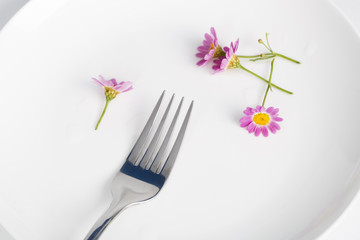 Fork and daisy in a white plate.