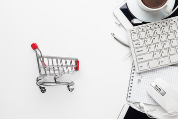 shopping online concept. small red trolley, different gadgets and stationery on the white office...
