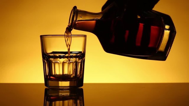 Whiskey or pour or skotch glass is pouring from a bottle. Taking a reverse movement
