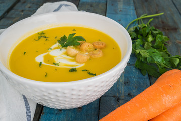 Carrot soup with cream and parsley on wooden background