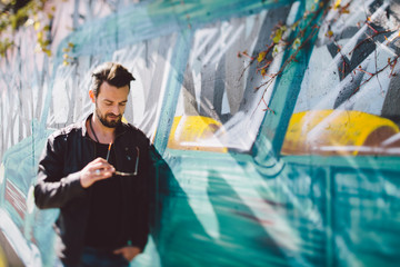 Man with leather jacket leaning on graffiti wall