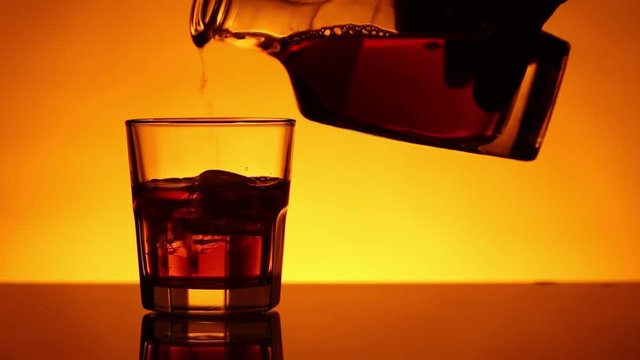 Whiskey or pour or skotch glass with ice is pouring from a bottle. Reverse movement