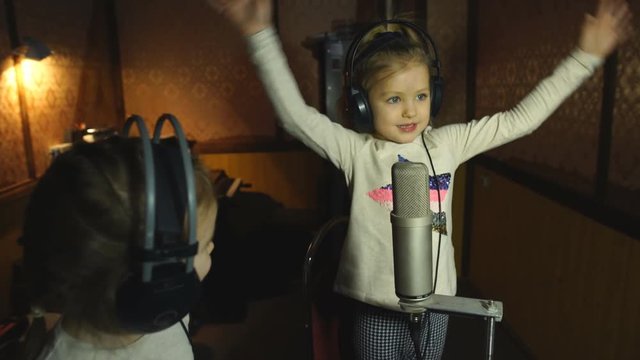 two little girls in headphones singing in microphone